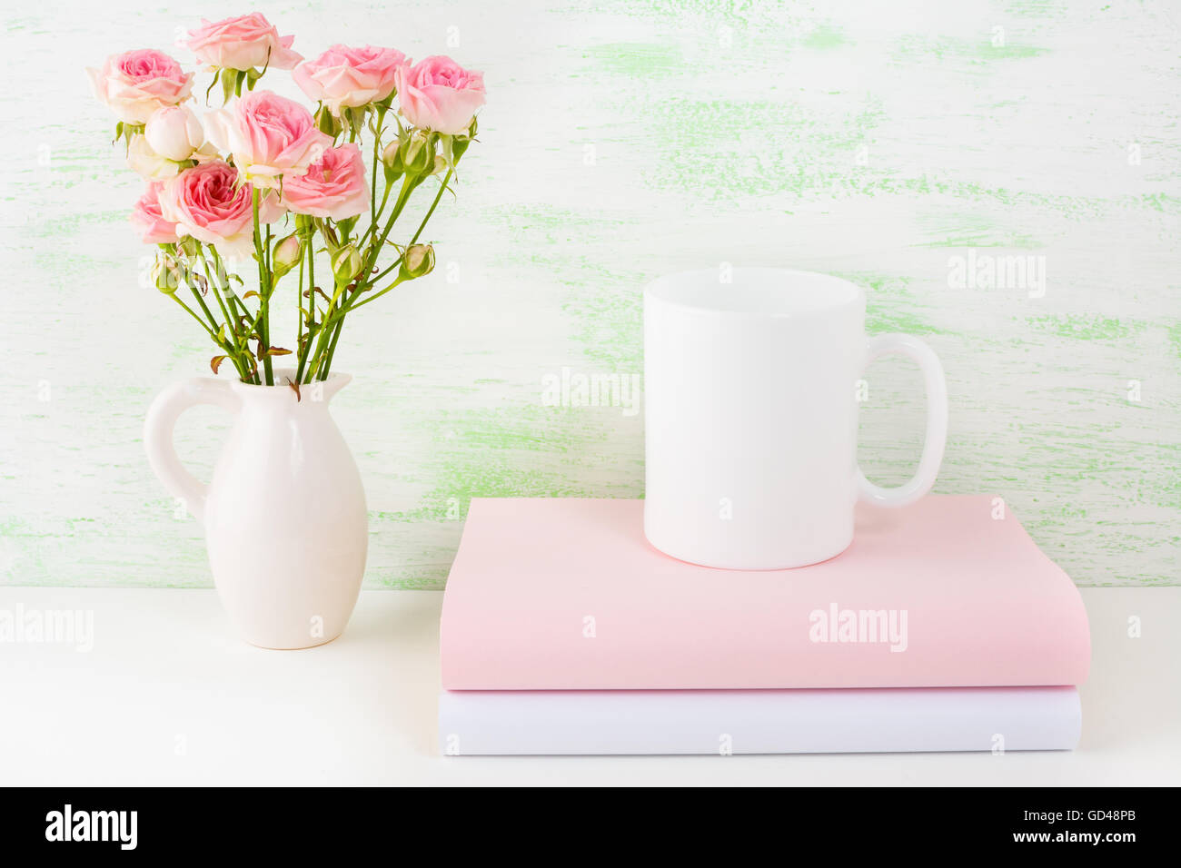 Coffee mug mockup with books and pink roses. Coffee cup mock-up for brand promotion.  Empty mug mockup for design presentation. Stock Photo