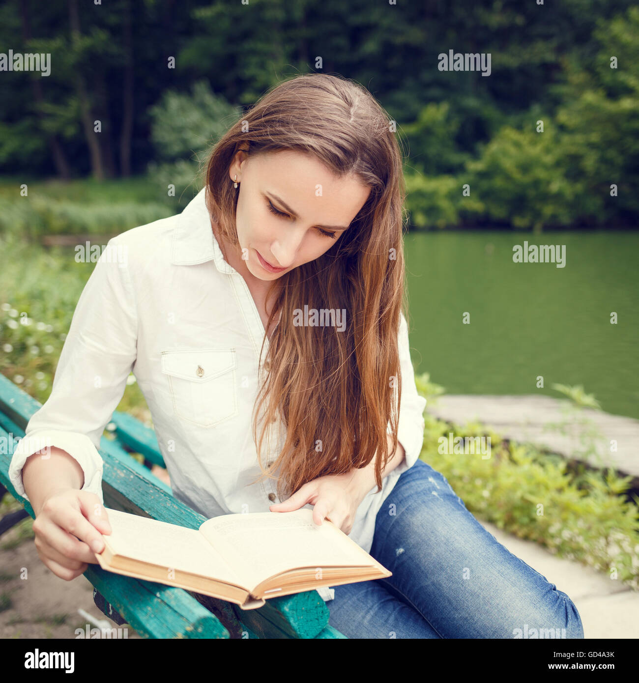 Young woman sitting on the bench in a park and reading a book ...