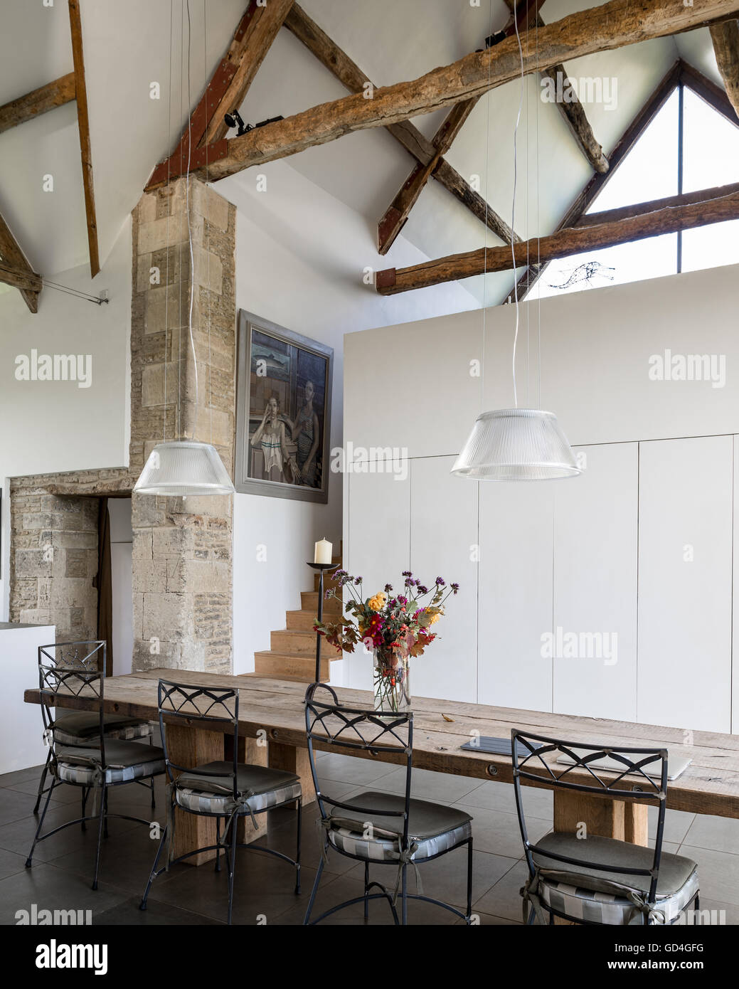 Timber-framed beamed ceiling above refectory style table in double-height barn conversion Stock Photo
