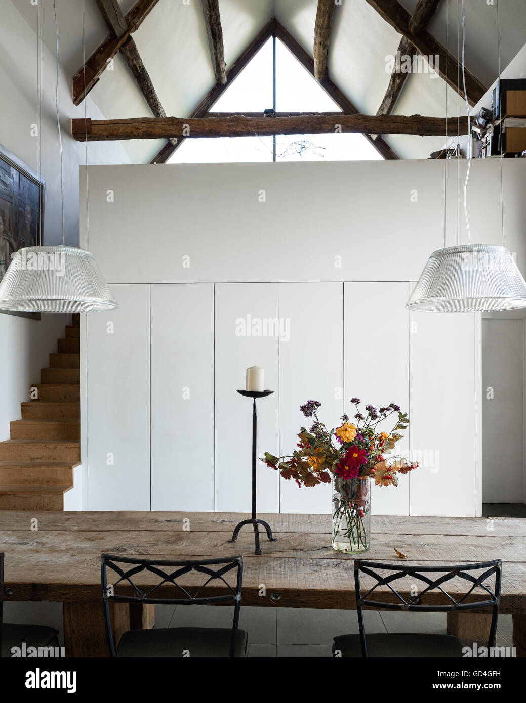 Timber-framed ceiling above refectory style table in double-height barn conversion Stock Photo