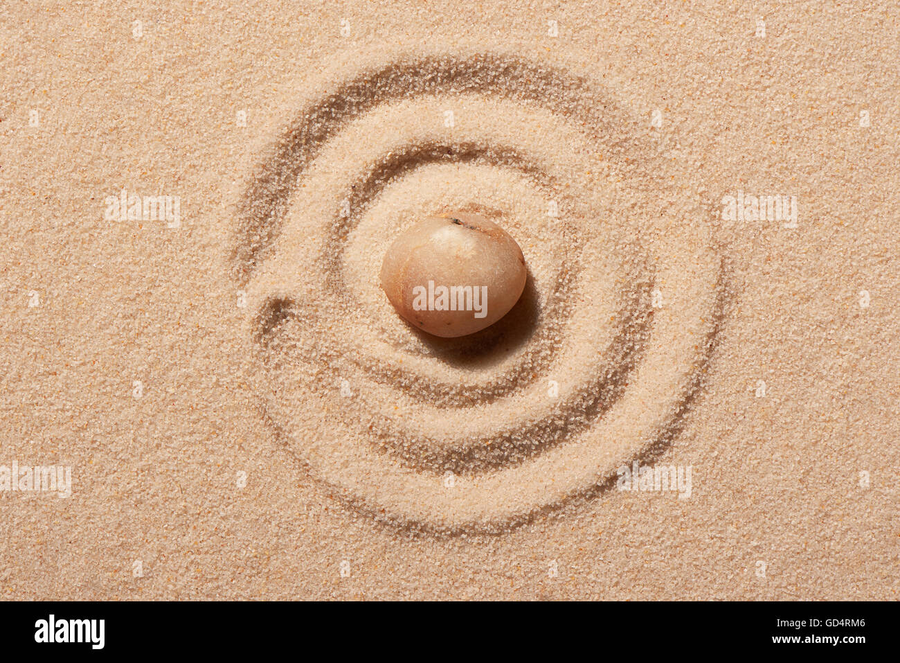 Spiral drawn on beach sand with pink round sea stone in centre. Summer ...