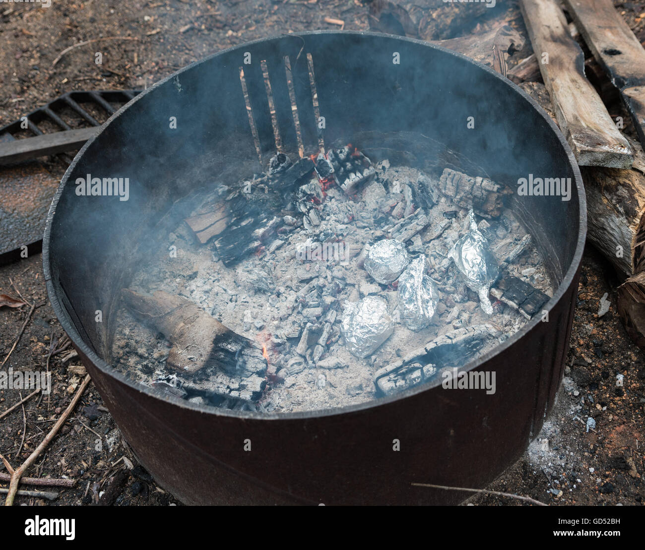 Potatoes wrapped in foil cooking on coals in camp fire Stock Photo