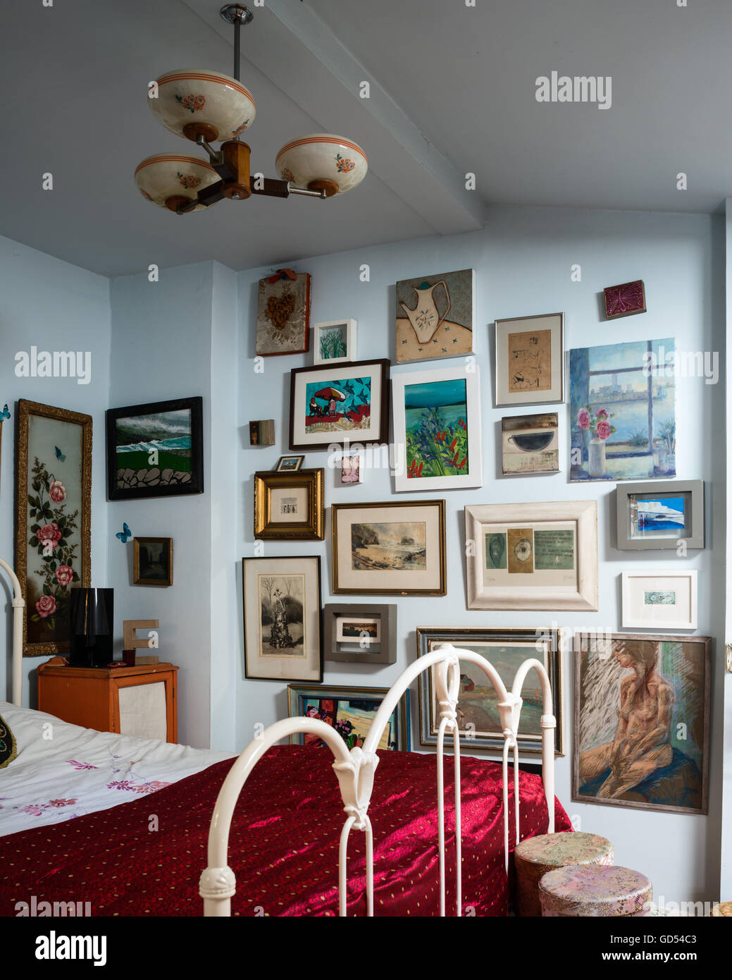 Assorted artworks on wall of bedroom with iron bedstead Stock Photo