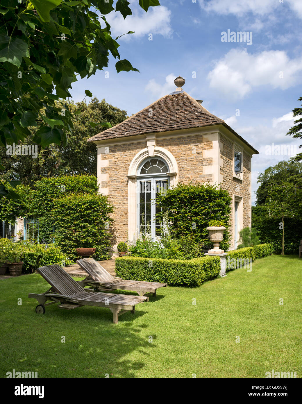 External facade of converted coach house with teak loungers on lawn with yew hedge. Stock Photo