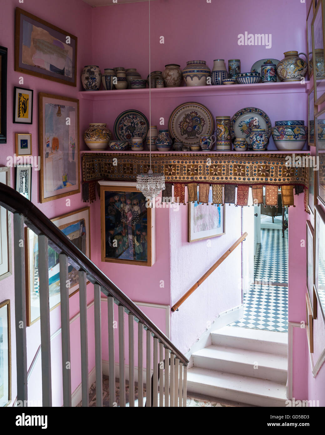 Collection of Poole pottery on shelves in pink stairwell with assorted artwork on walls Stock Photo