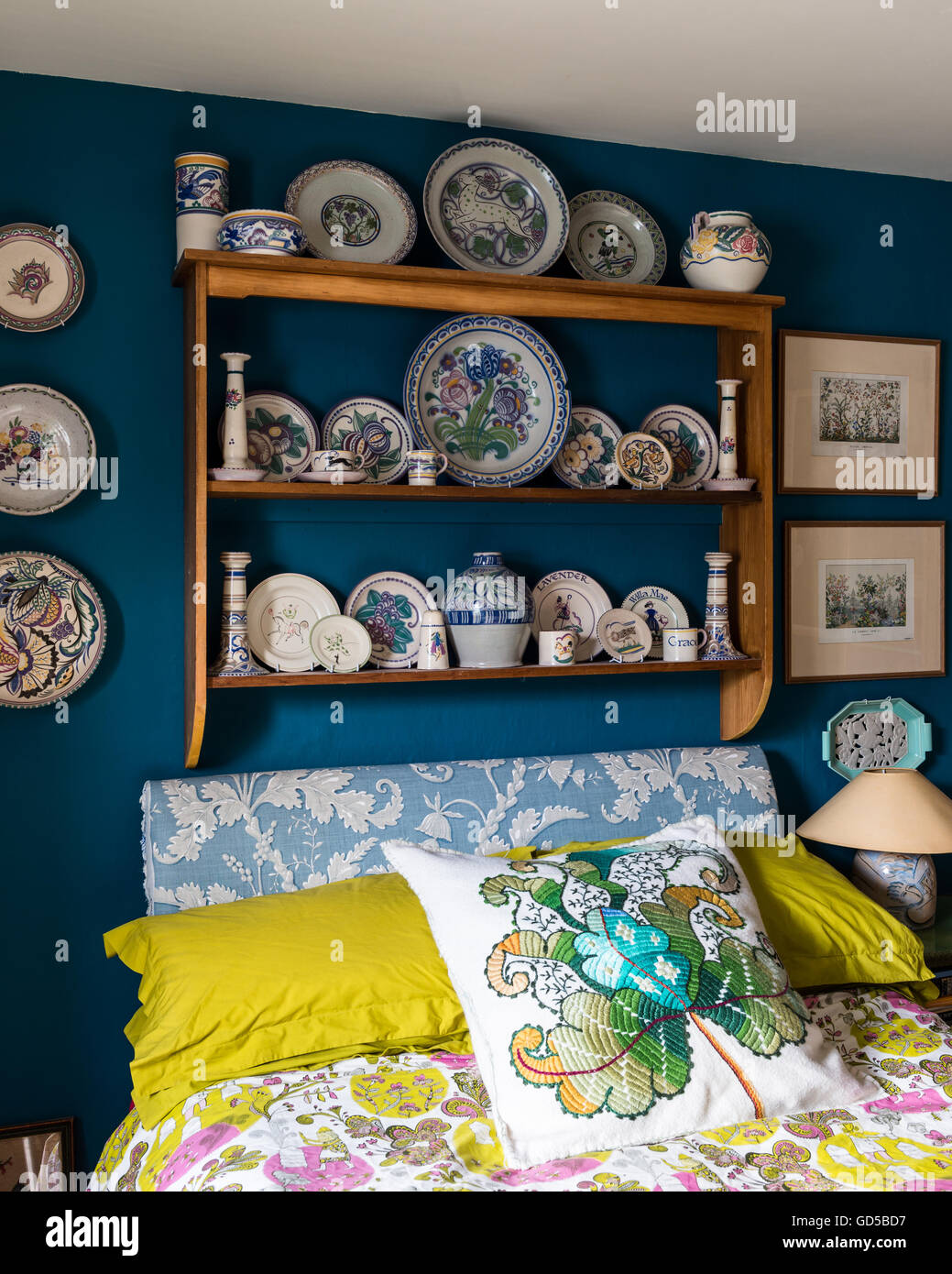 Poole pottery displayed on wooden shelf in bedroom painted in Deep Space Blue by Little Greene.The bed is upholstered and cover Stock Photo