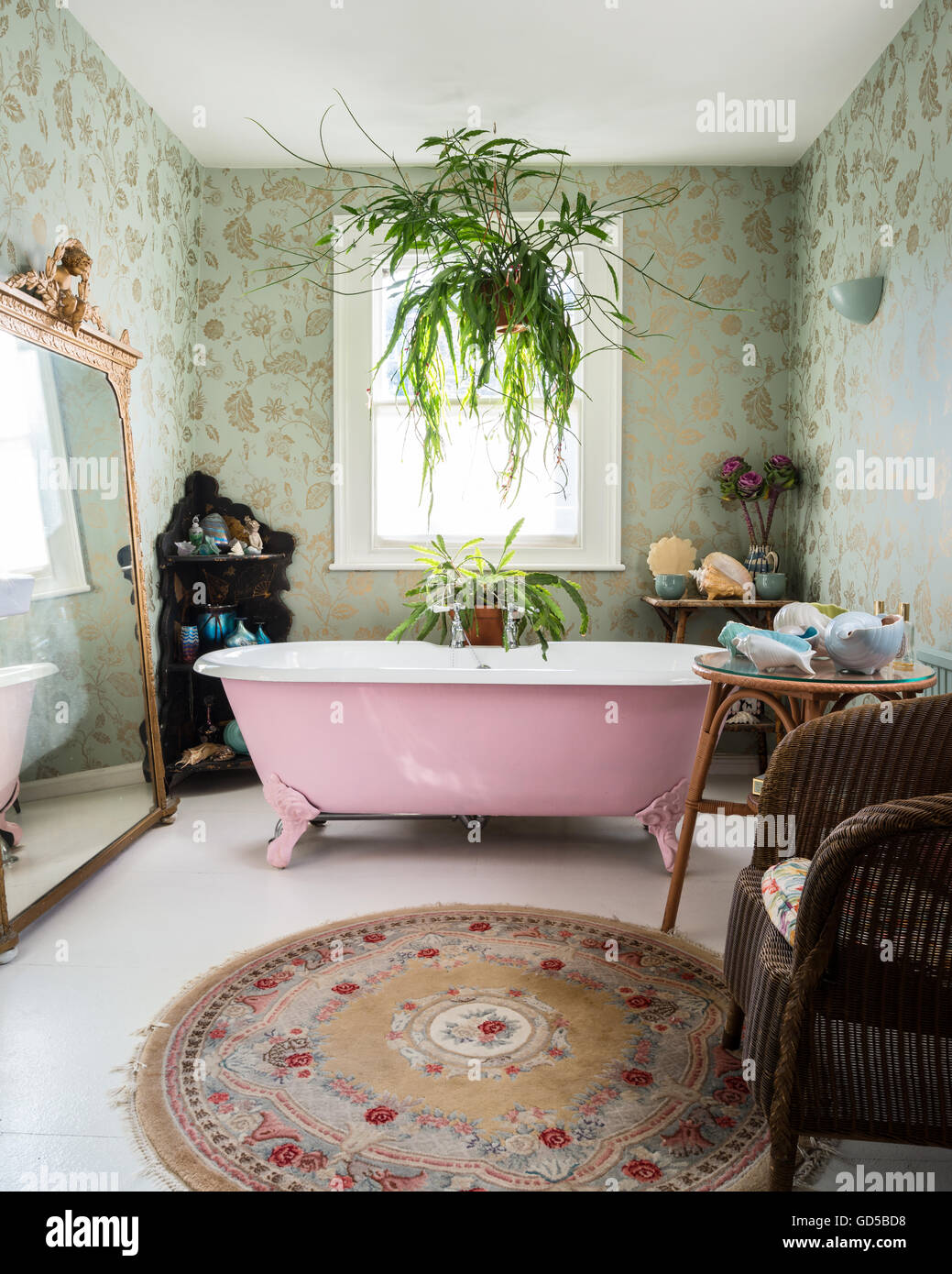Pink double ended, roll top, freestanding bath in bathroom with Colefax & Fowler print wallpaper and large giltwood mirror Stock Photo