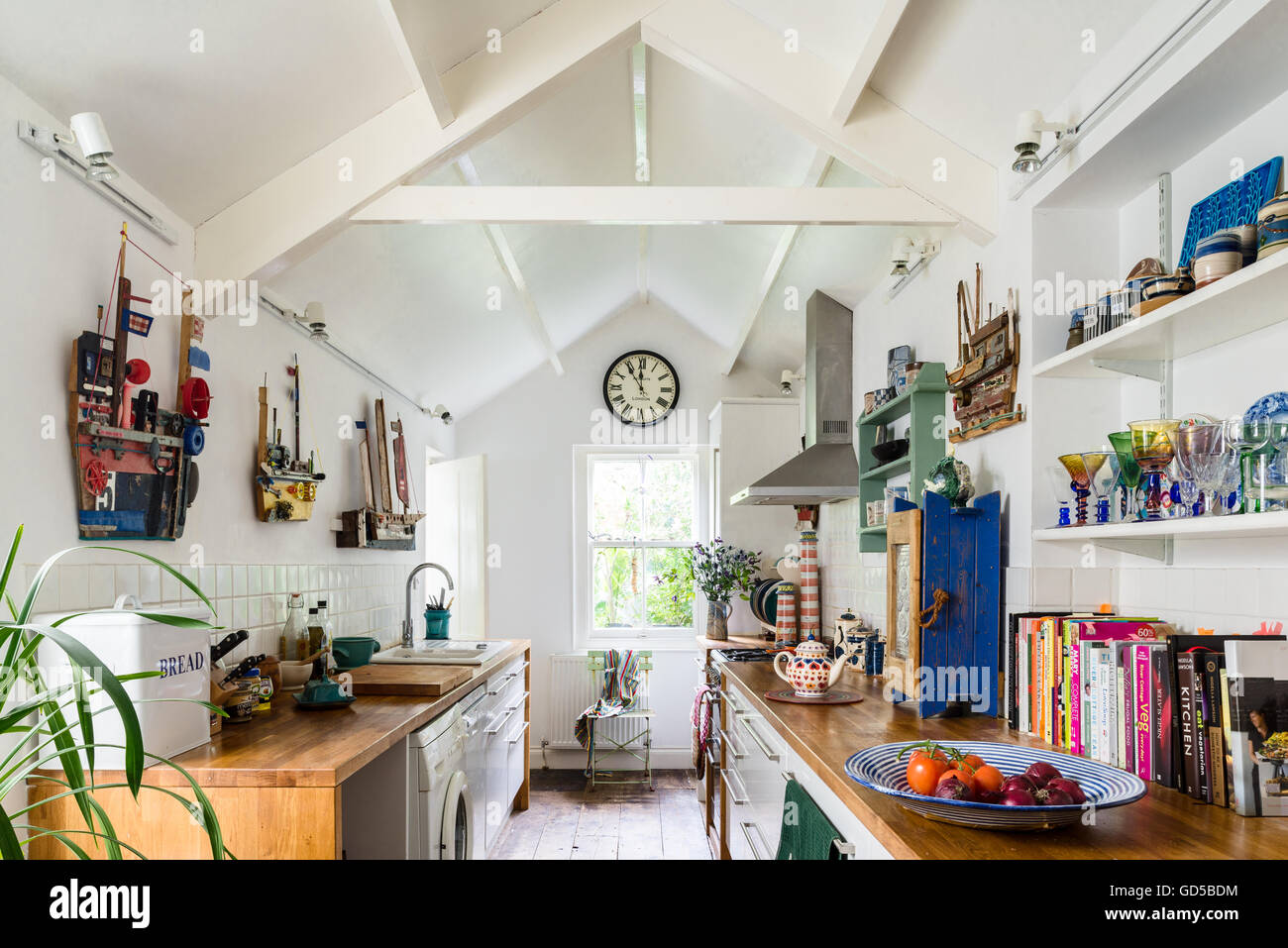 Galley style white kitchen with pitched roof, wooden worktops and open shelving. The walls are adorned with boats made by Rachel Stock Photo