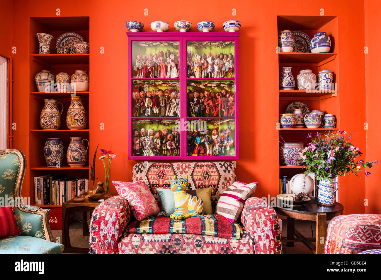 Club sofa upholstered in kilim material beneath glass-fronted pink cabinet containing collection of marionette puppets. Stock Photo