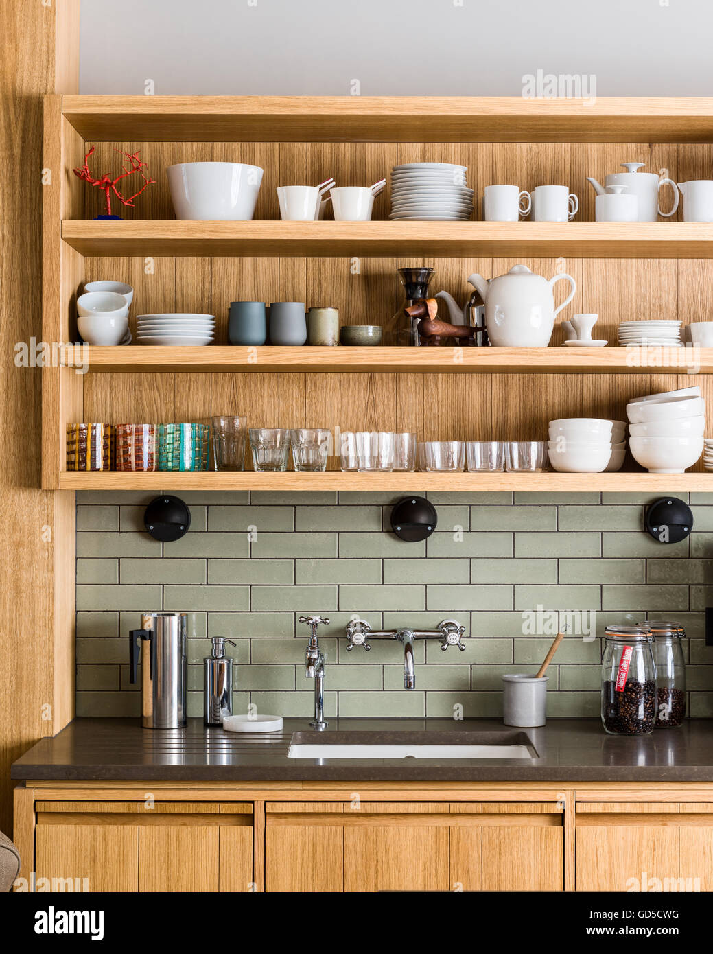 White crockery on custom-made open oak shelving by Bohemian Works above Silestone worktop and sink Stock Photo