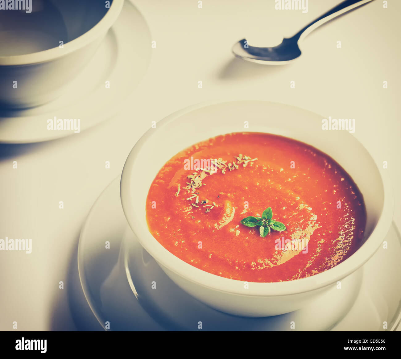 Vintage toned photo of a white bowl with tomato cream soup with basil leaves on top. Stock Photo