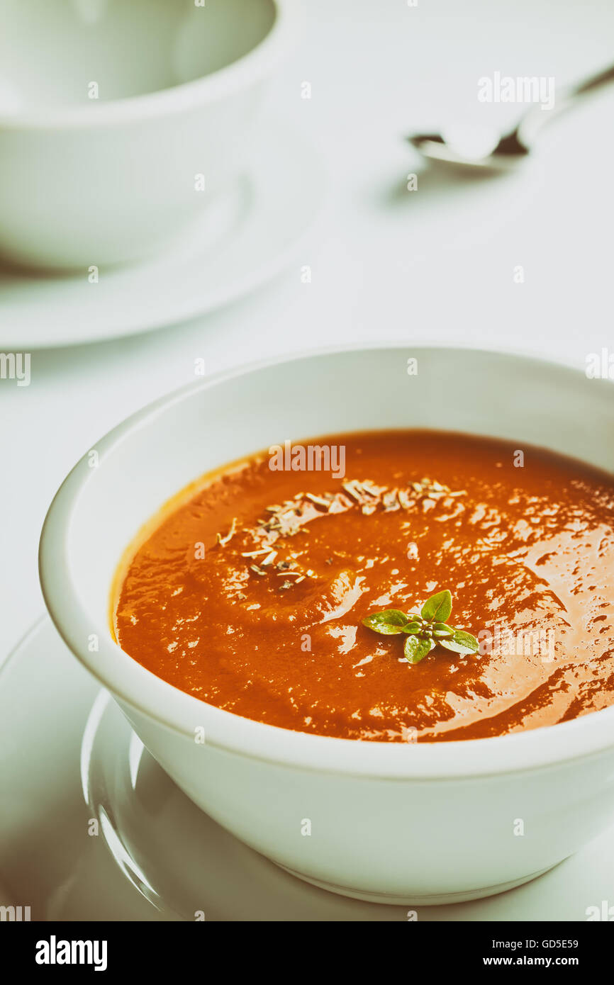 Retro stylized photo of a white bowl with tomato cream soup with basil leaves on top. Stock Photo