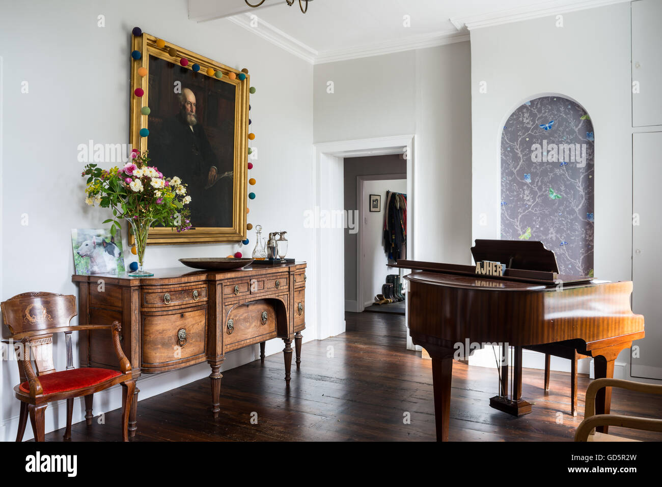 Large portrait above mahogany sideboard in hall with baby grand piano. Stock Photo