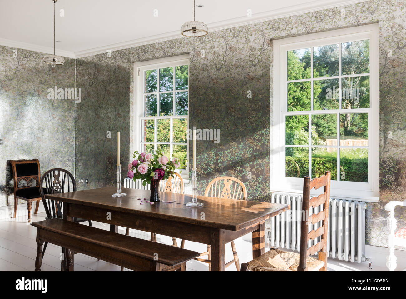 Oak refectory table in breakfast room with reflective foil wallpaper by Anna French. Stock Photo