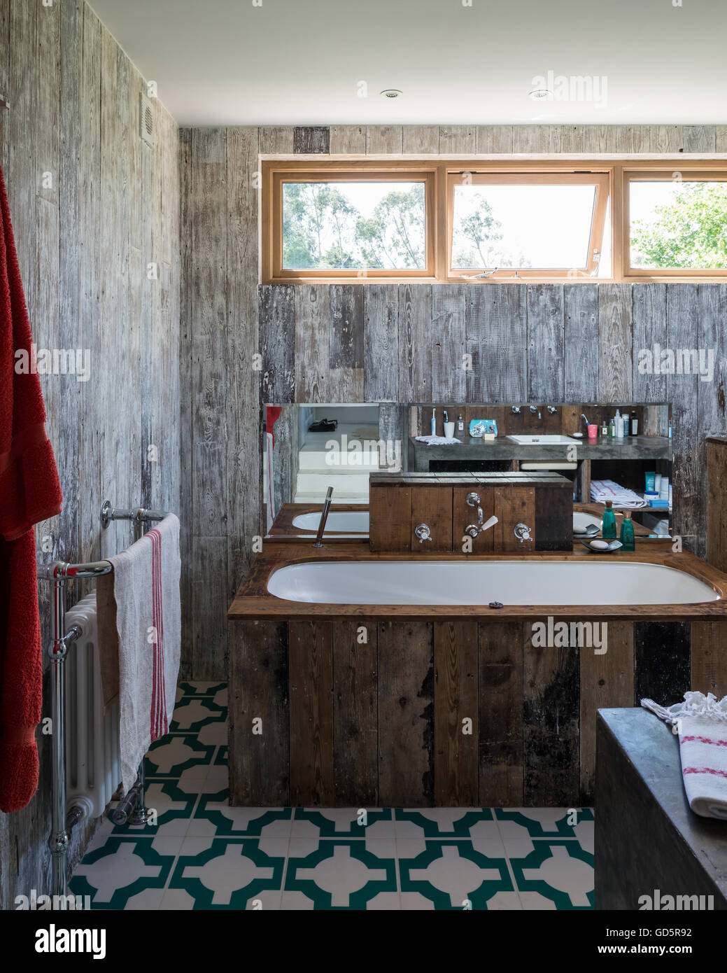 Bath tub clad in recycled floorboards in bathroom with Parquet Turquoise vinyl floor tiles by Neisha Crosland Stock Photo