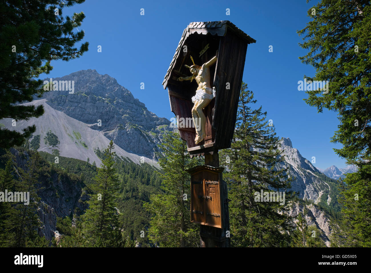 wooden Jesus Christ on cross in sunlight with mountain background, Karwendel, Germany Stock Photo