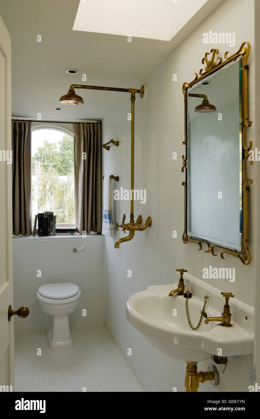 Brass shower, tap fittings and mirror surround in white tiled bathroom Portland Road, London, UK Stock Photo