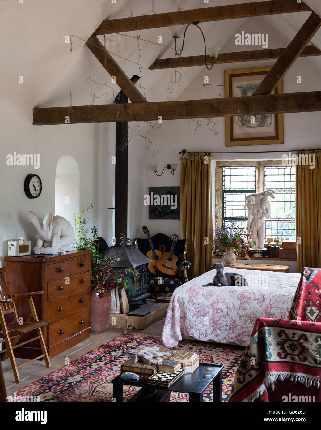 Bright kelim in airy bedroom with ceilings beams, woodburning stove and Sophie ryder sculptures Stock Photo