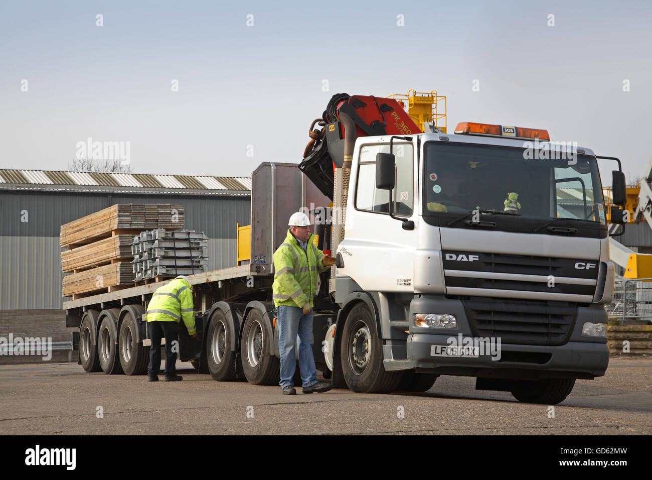 A driver opens the door of his partially loaded articulated lorry whilst a colleague checks the trailer Stock Photo