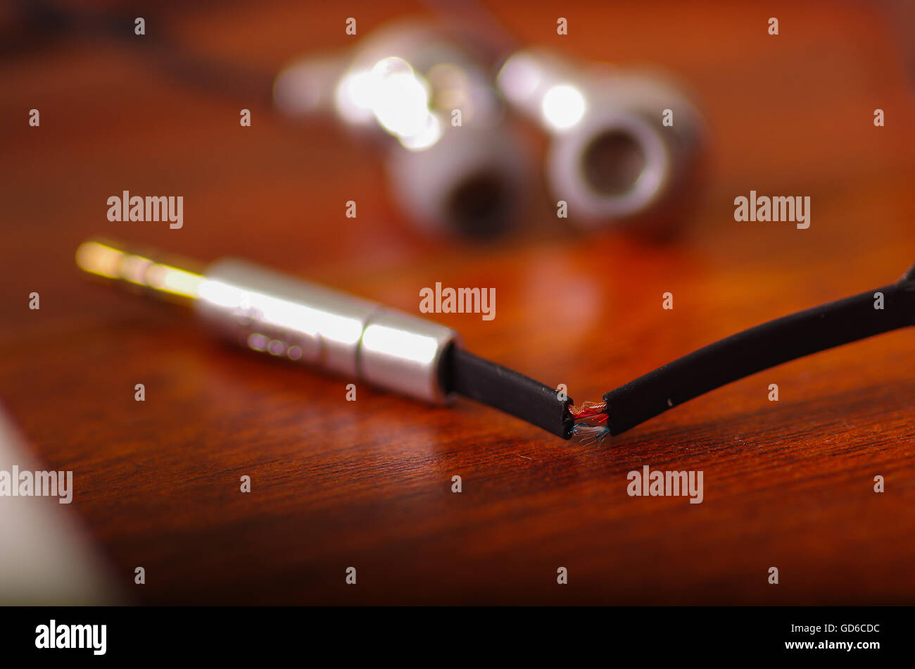 Broken audio headphones cable lying on wooden surface, part of internal wire exposed through