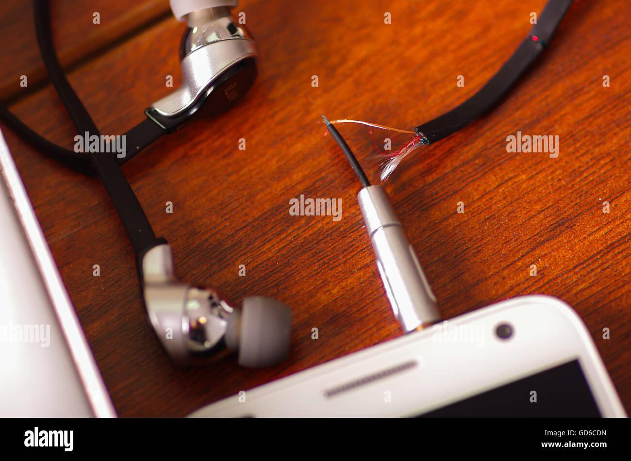 Broken audio headphones cable connected into smartphone lying on wooden surface, part of wire