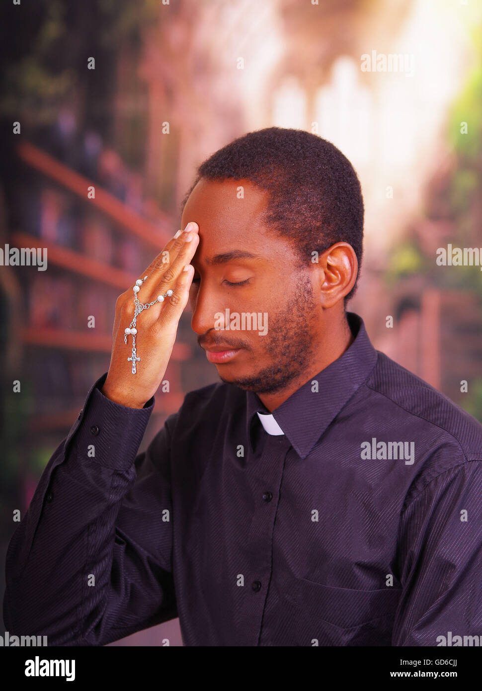 Catholic priest wearing traditional clerical collar shirt standing performing sign of the cross and holding rosary in hand, religion concept Stock Photo