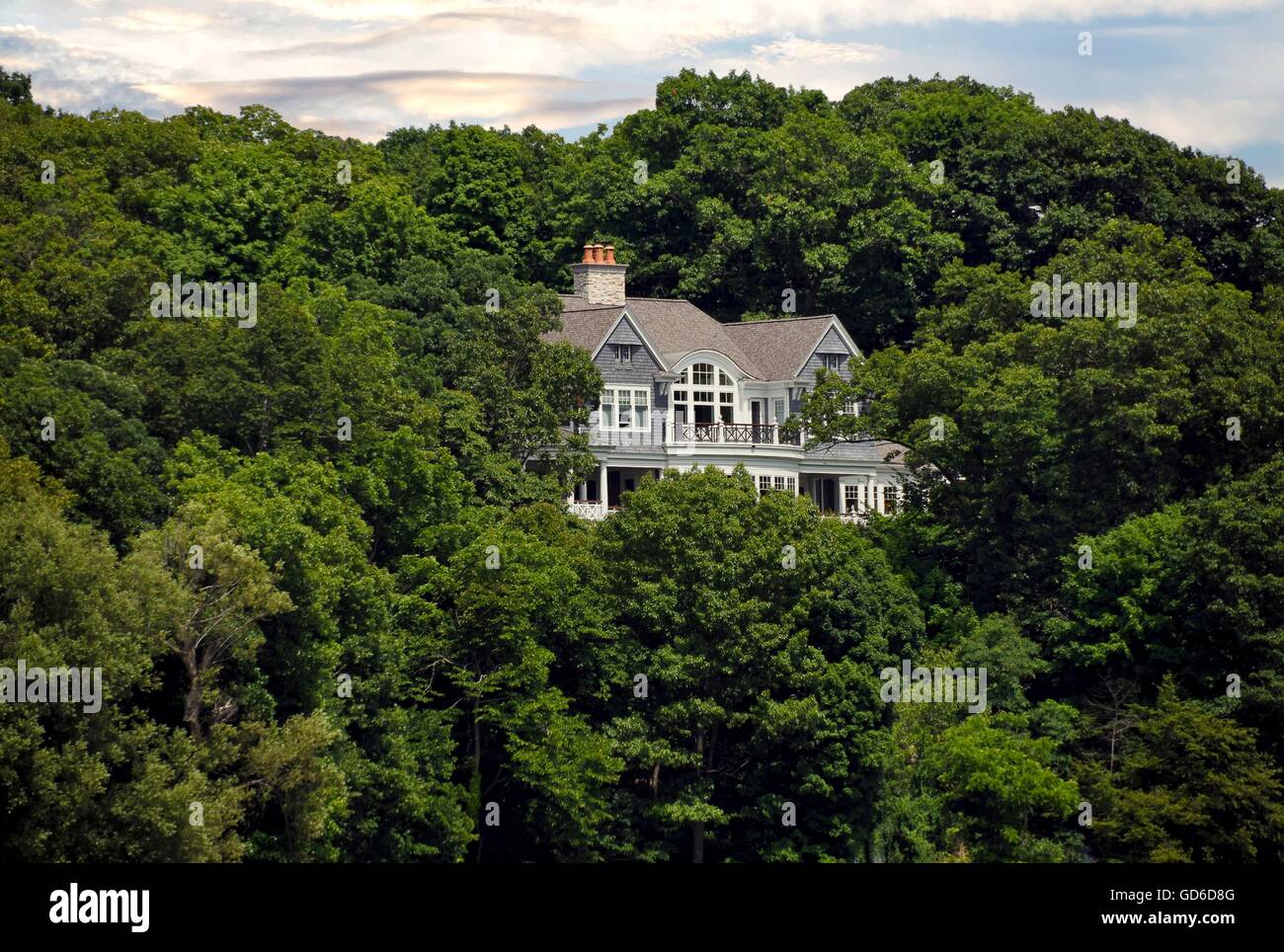 Luxury home in lush summer tree foliage on a hill. Stock Photo