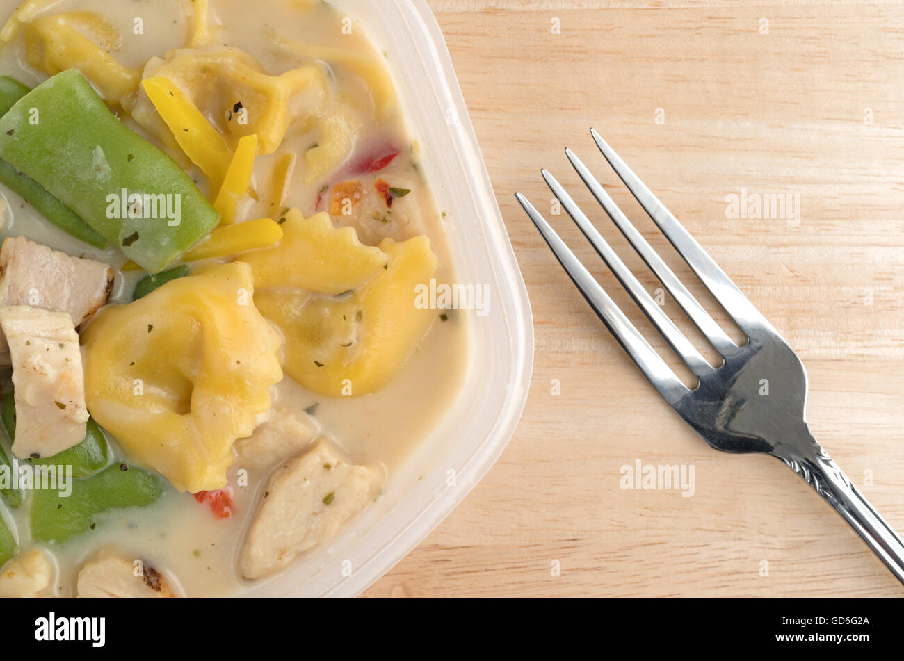 Top close view of a chicken with tortellini and vegetable TV dinner in a plastic tray with a fork to the side atop a wood table. Stock Photo