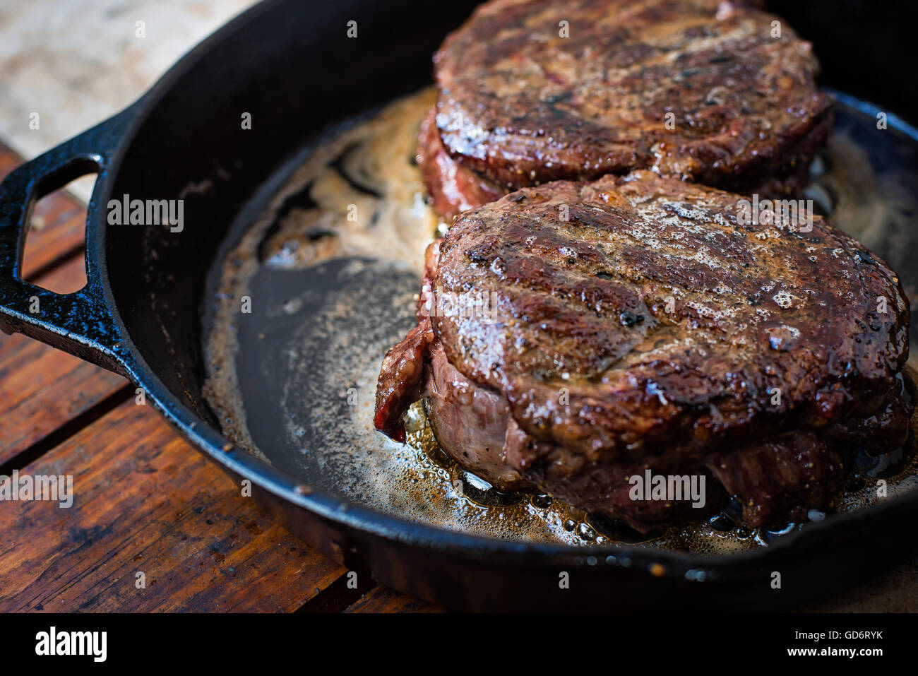 A pair of ribeye cap steaks cooked in a cast iron skillet along with a butter bath. Stock Photo