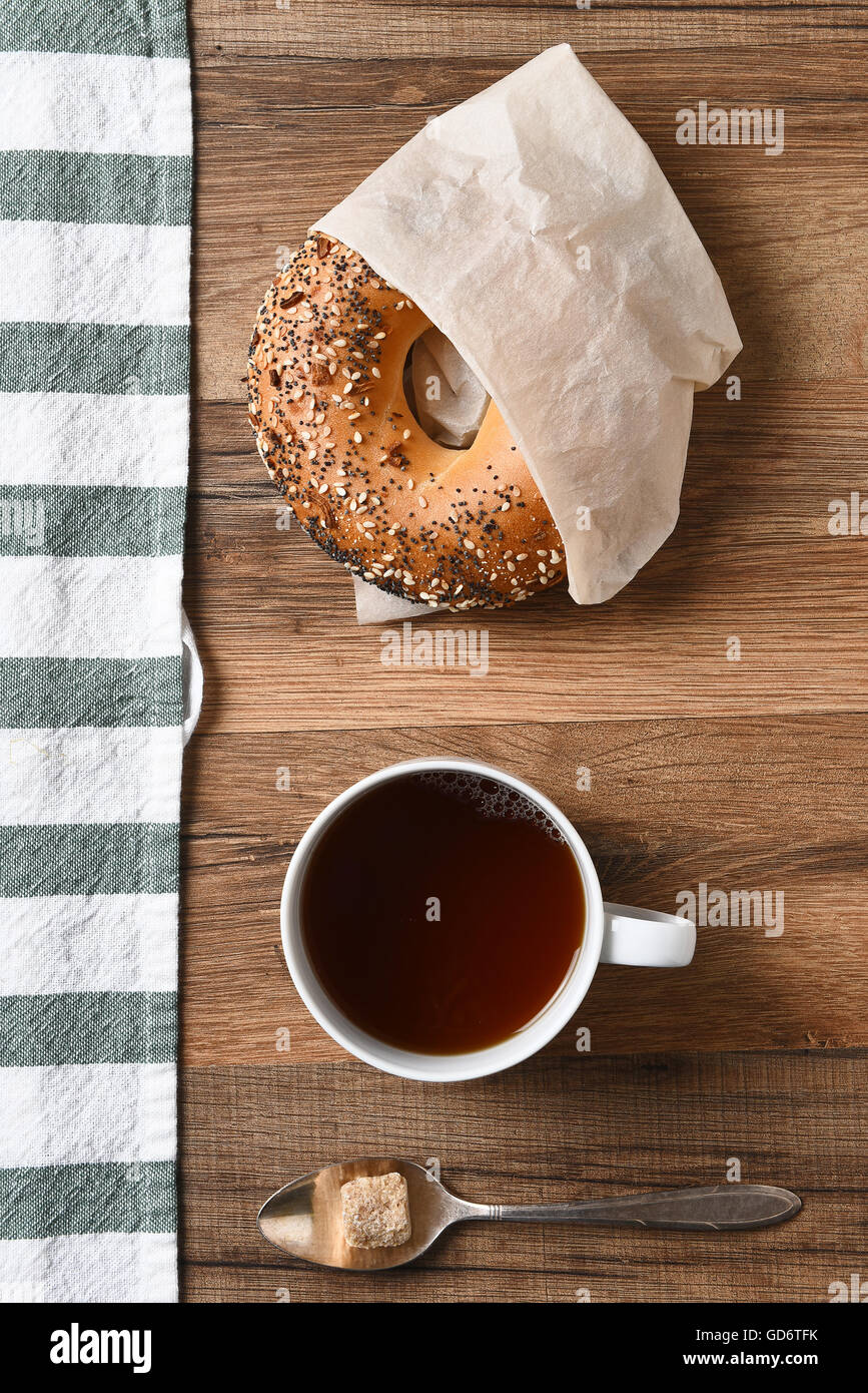 High angle view of a bagel, cup of coffee, and spoon with raw sugar lump with a striped towel. Stock Photo