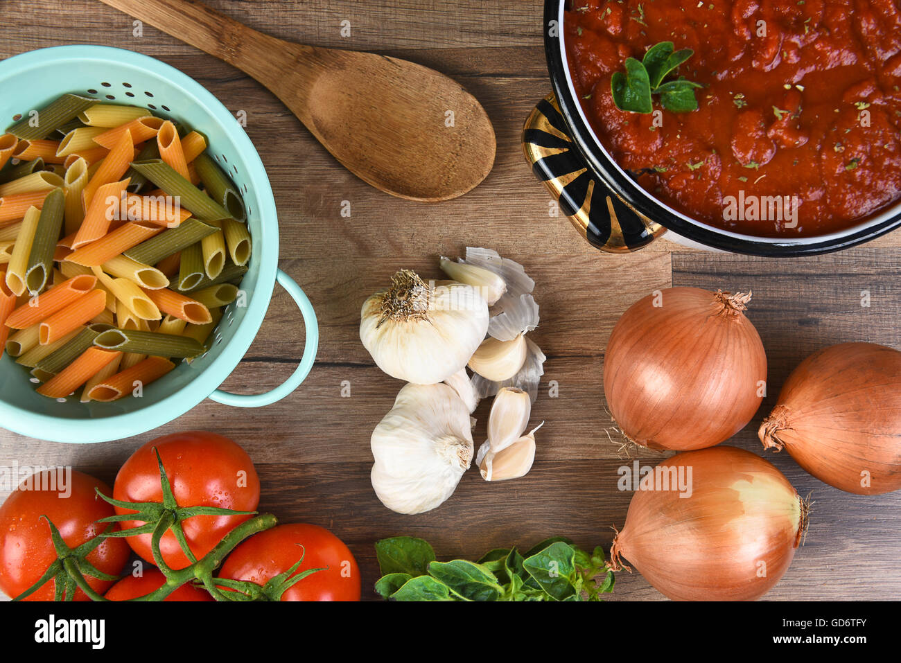 Italian meal ingredients on a wood kitchen table. A pot of sauce, colander of rigatoni, tomatoes, garlic, oregano, and onions Stock Photo