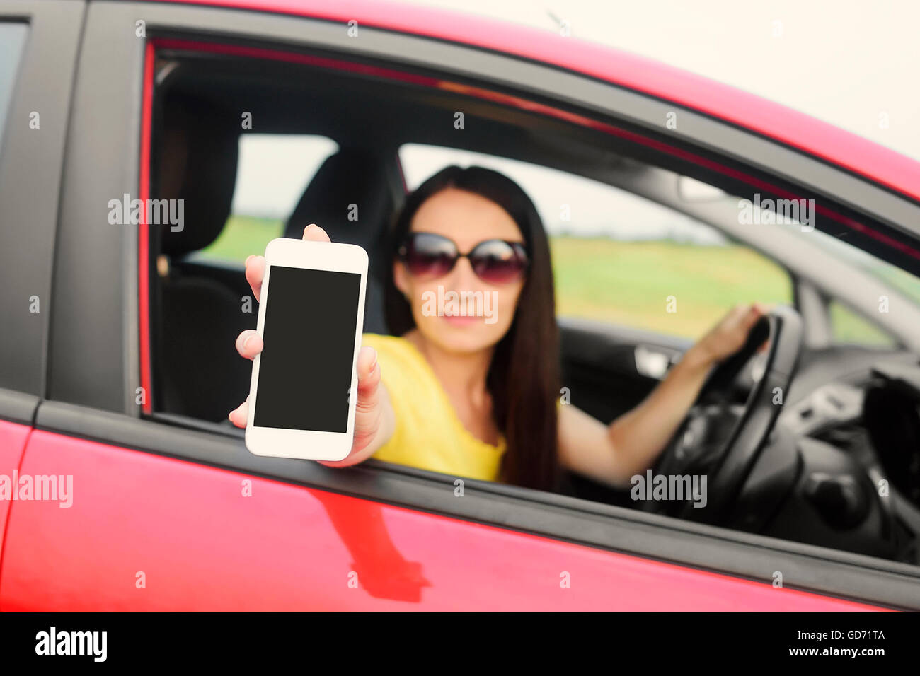 Woman showing her smartphone out the window of a car. Stock Photo
