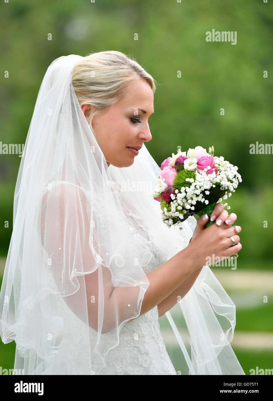Bride in wedding dress with veil looking at bridal bouqet, Germany Stock Photo