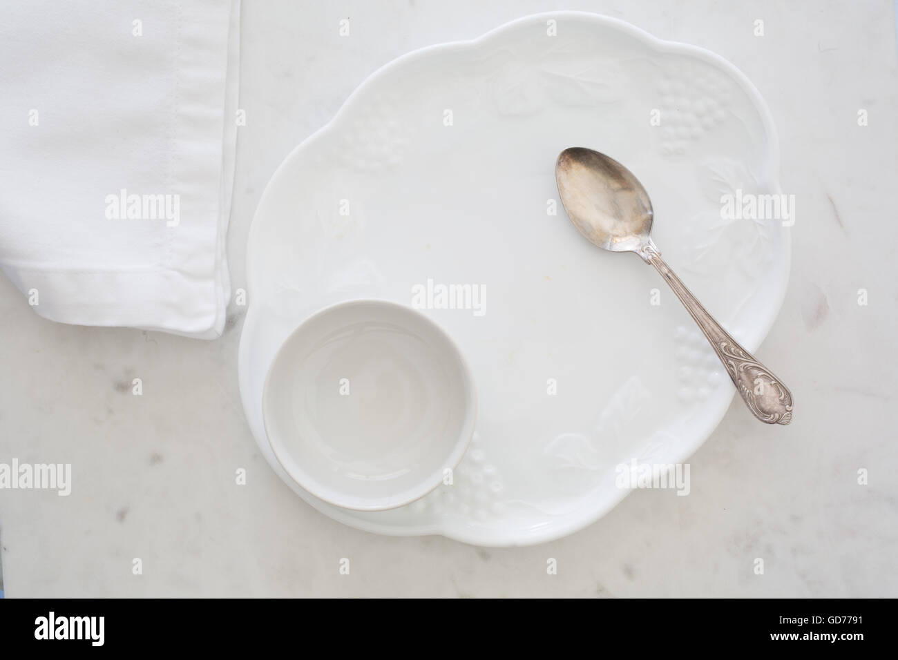 Top-down view of white dessert plate, bowl, napkin and elegant silver spoon on white marble Stock Photo