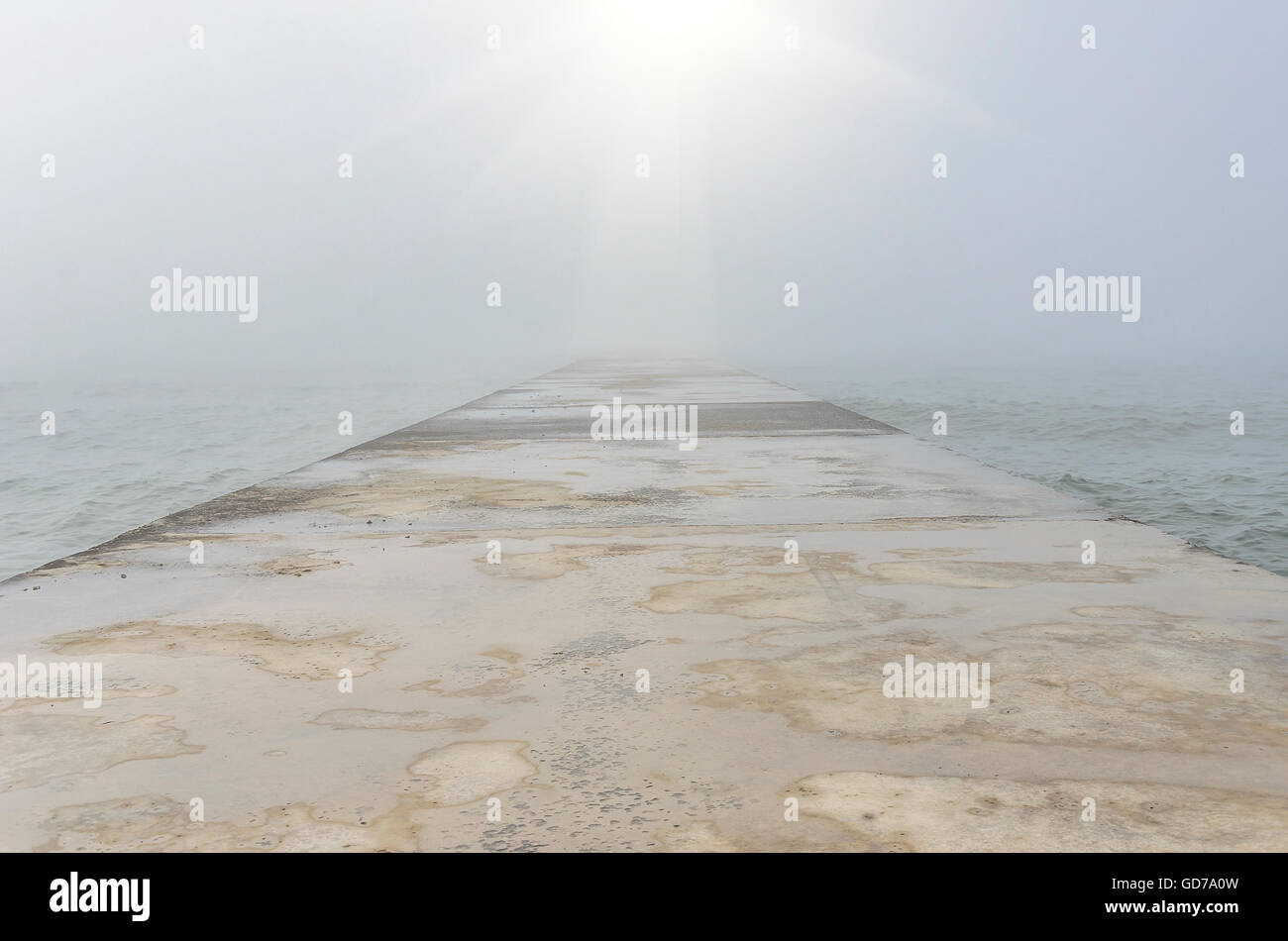 Concrete pier goes away into the sea in a foggy day. Stock Photo