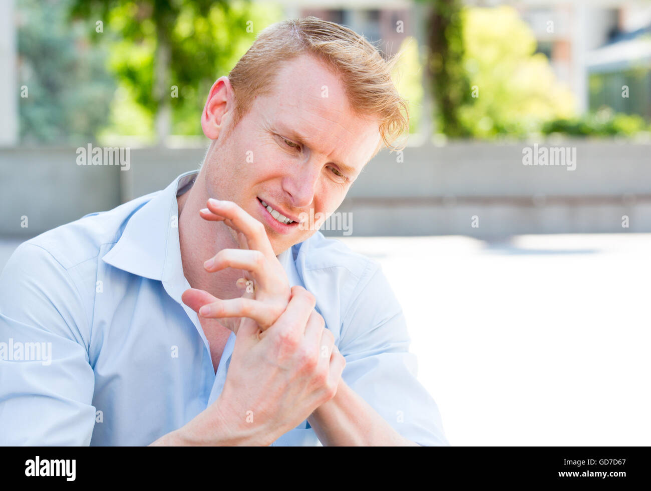 Closeup portrait, young man having acute bad joint pain in his hands, writer's cramp, massaging them, sitting in chair, isolated Stock Photo