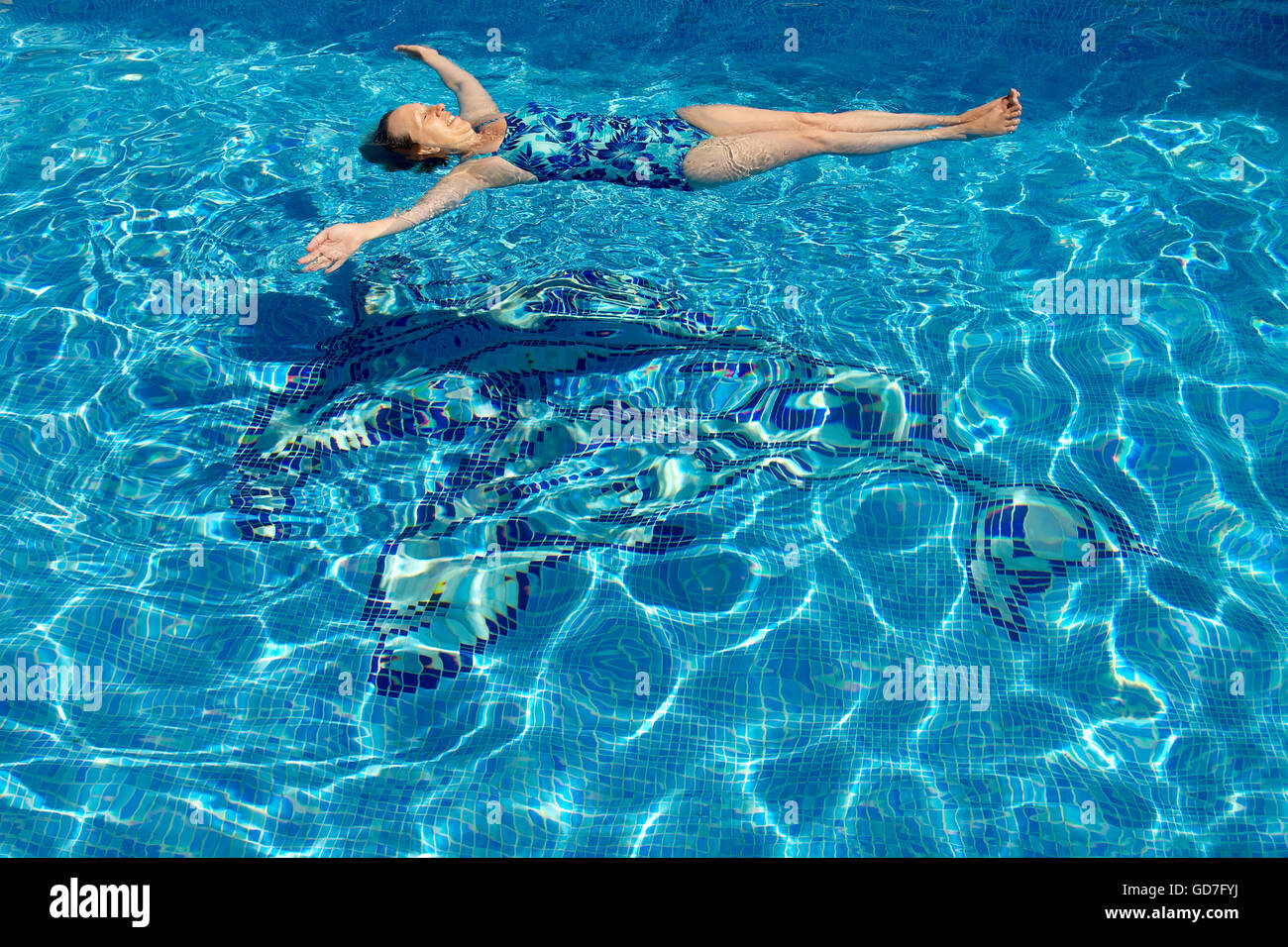 Woman floating in a swimming pool with dappled blue water. Stock Photo
