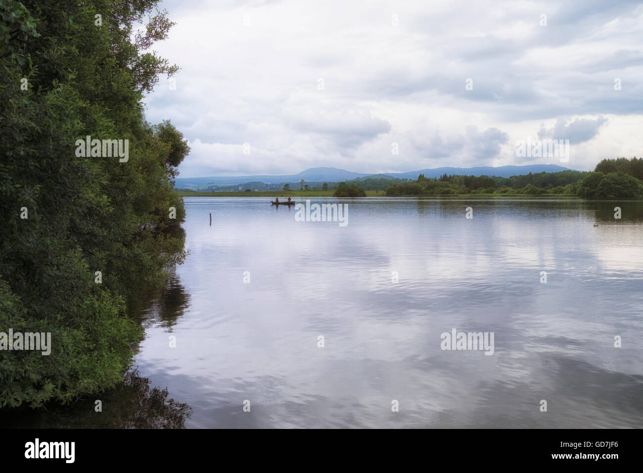 Peaceful scene of two men in a boat fishing in the calm waters of Lake of Menteith - Scotland's only loch. Stock Photo