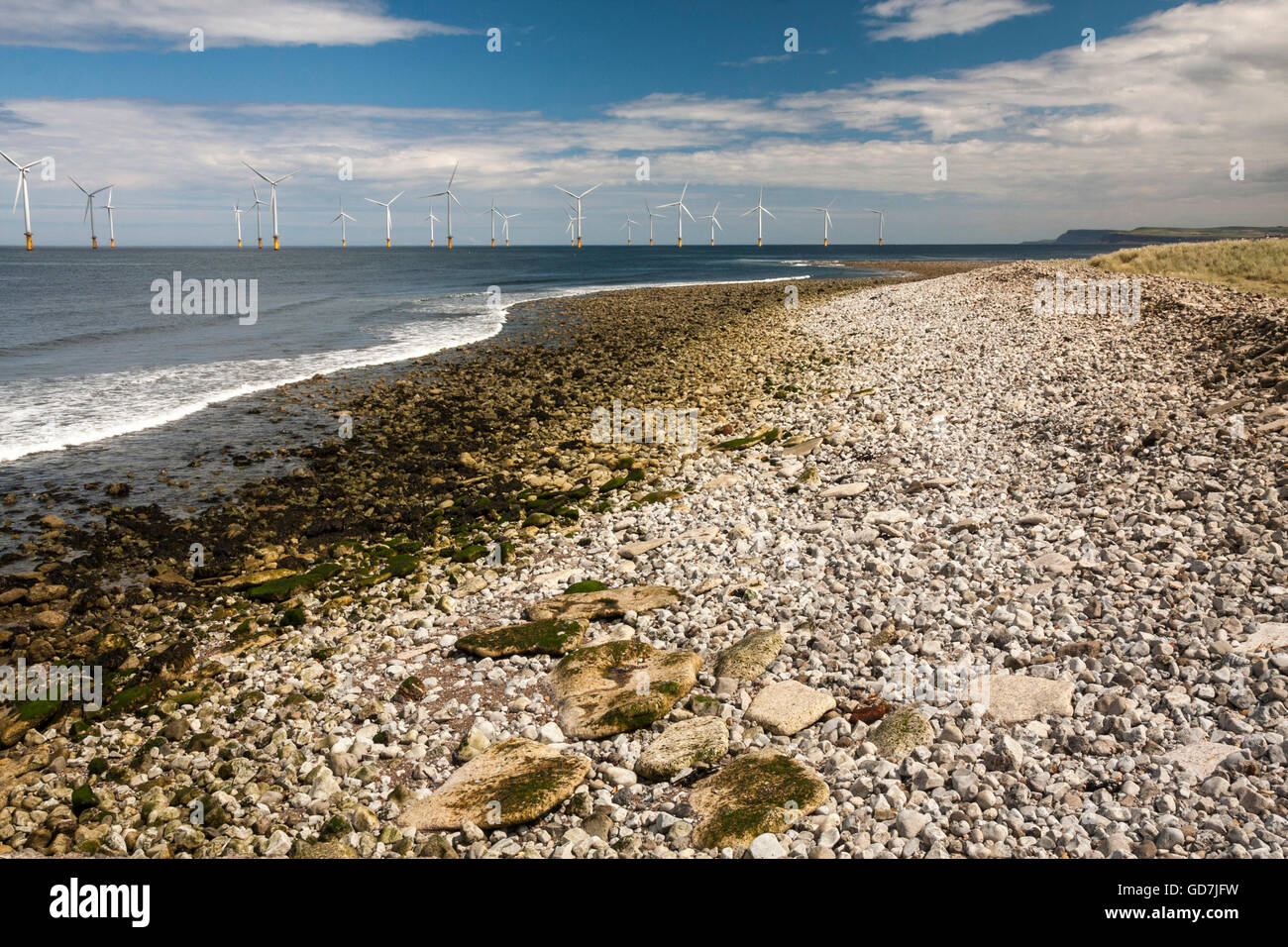 The rocky beach at Redcar in north east England with the offshore wind turbines and blue cloudy skies Stock Photo