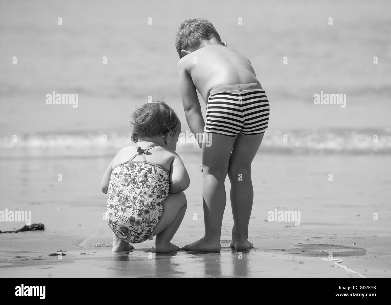 brother and sister family in the sand on holiday vacation discovering and exploring the beach black and white retro style Stock Photo