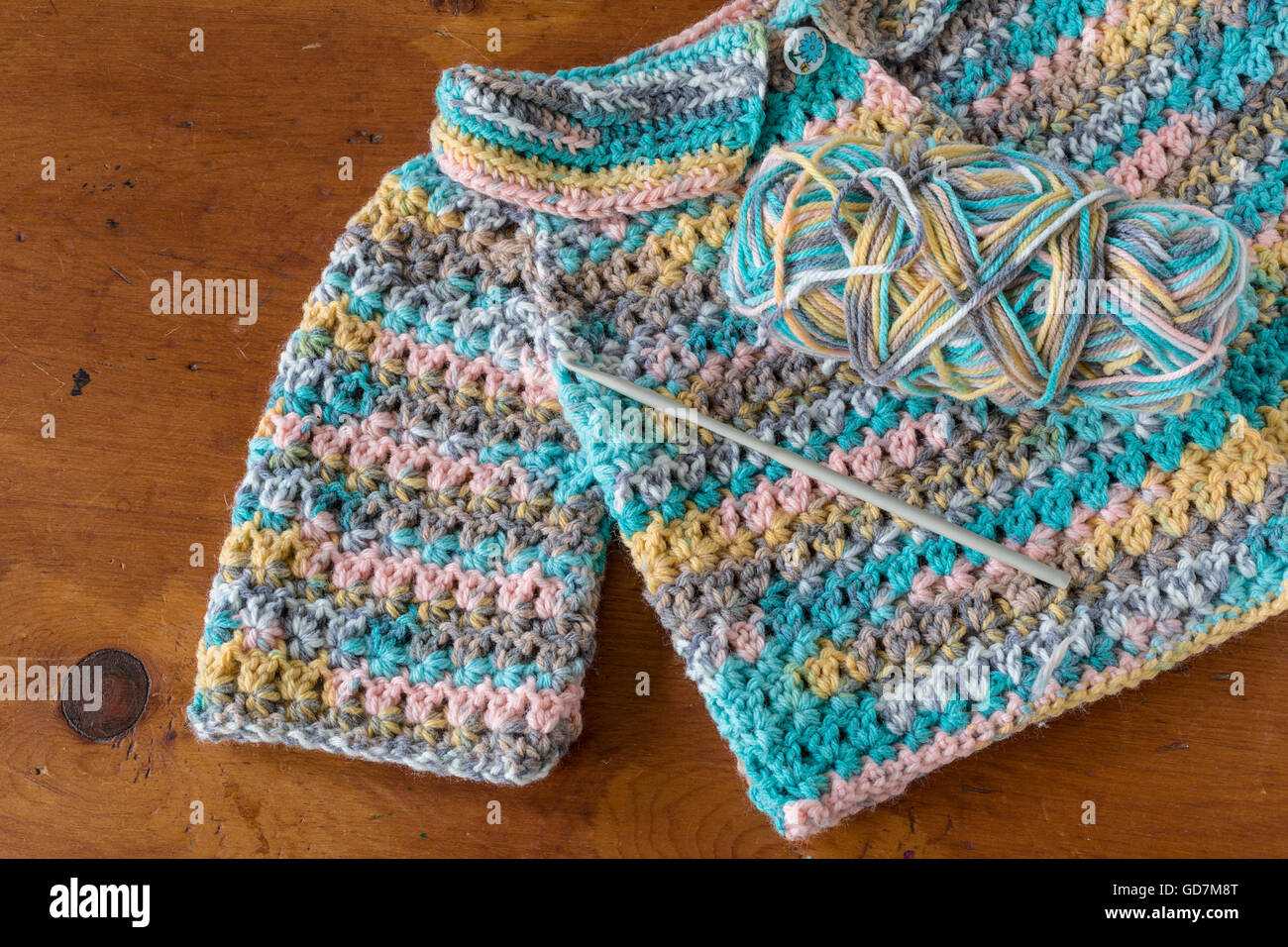 Crocheted baby sweater with a crochet hook and skein of yarn. Stock Photo