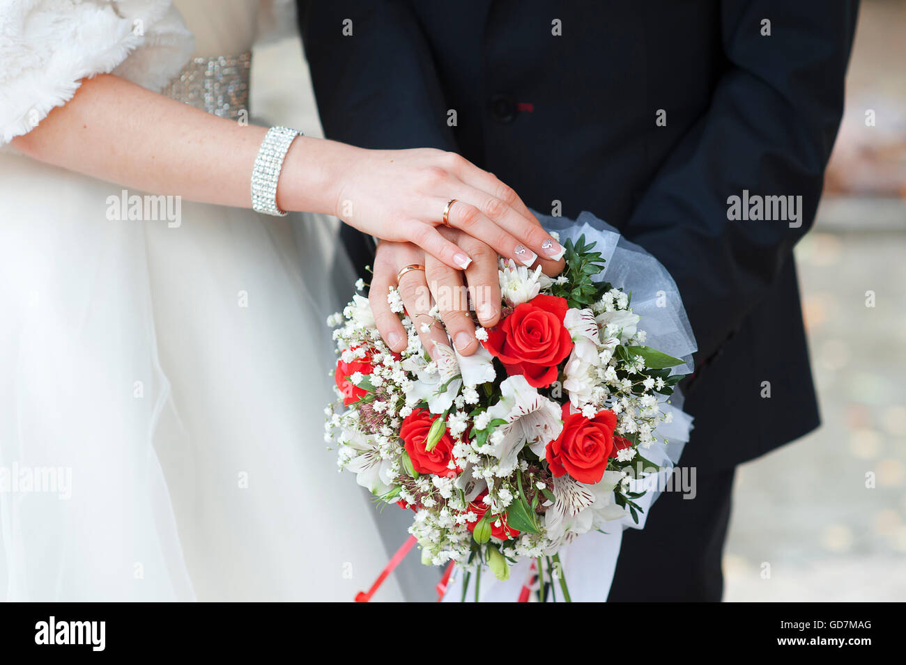 Hands of bride and groom with rings on wedding bouquet of roses Stock Photo