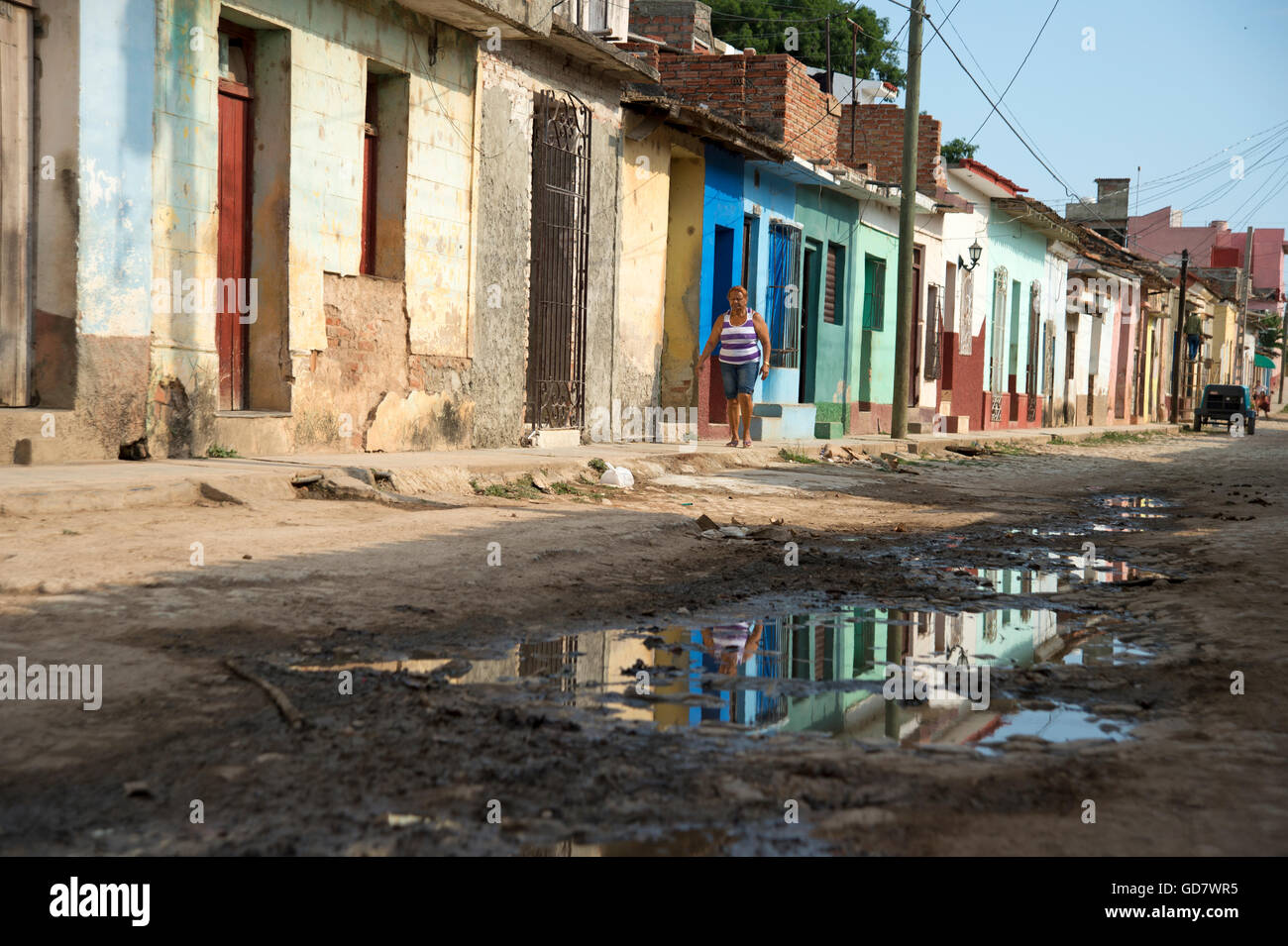 A Cuban woman walks along a neglected street of traditional houses in a rundown area of Trinidad Cuba Stock Photo