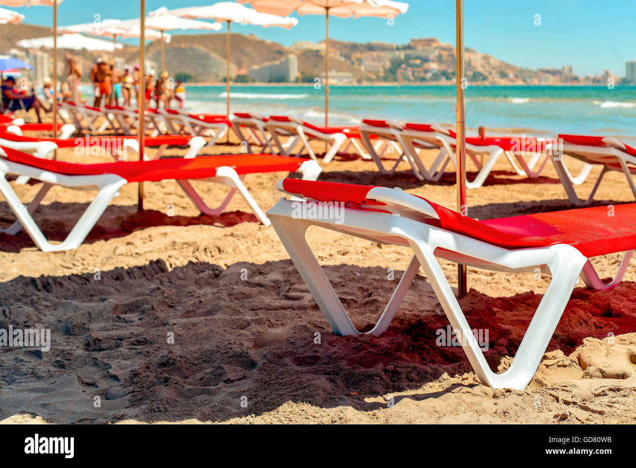 closeup of some sunloungers and umbrellas in San Antonio Beach in Cullera, Spain, with the Mediterranean sea and some unrecogniz Stock Photo