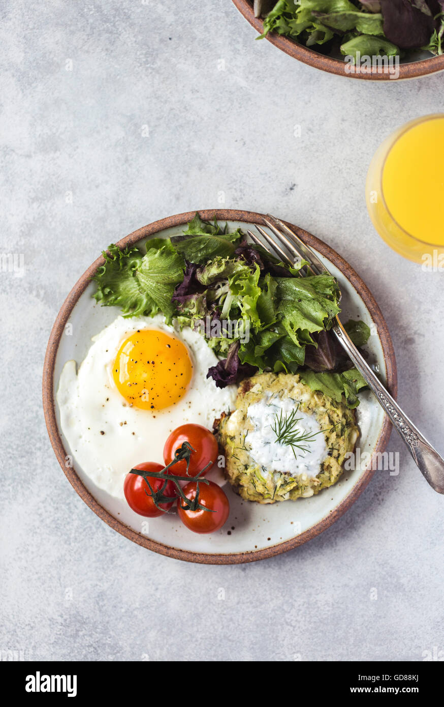 A fried egg, green salad, and a zucchini fritter are served on a plate photographed from the top. Stock Photo
