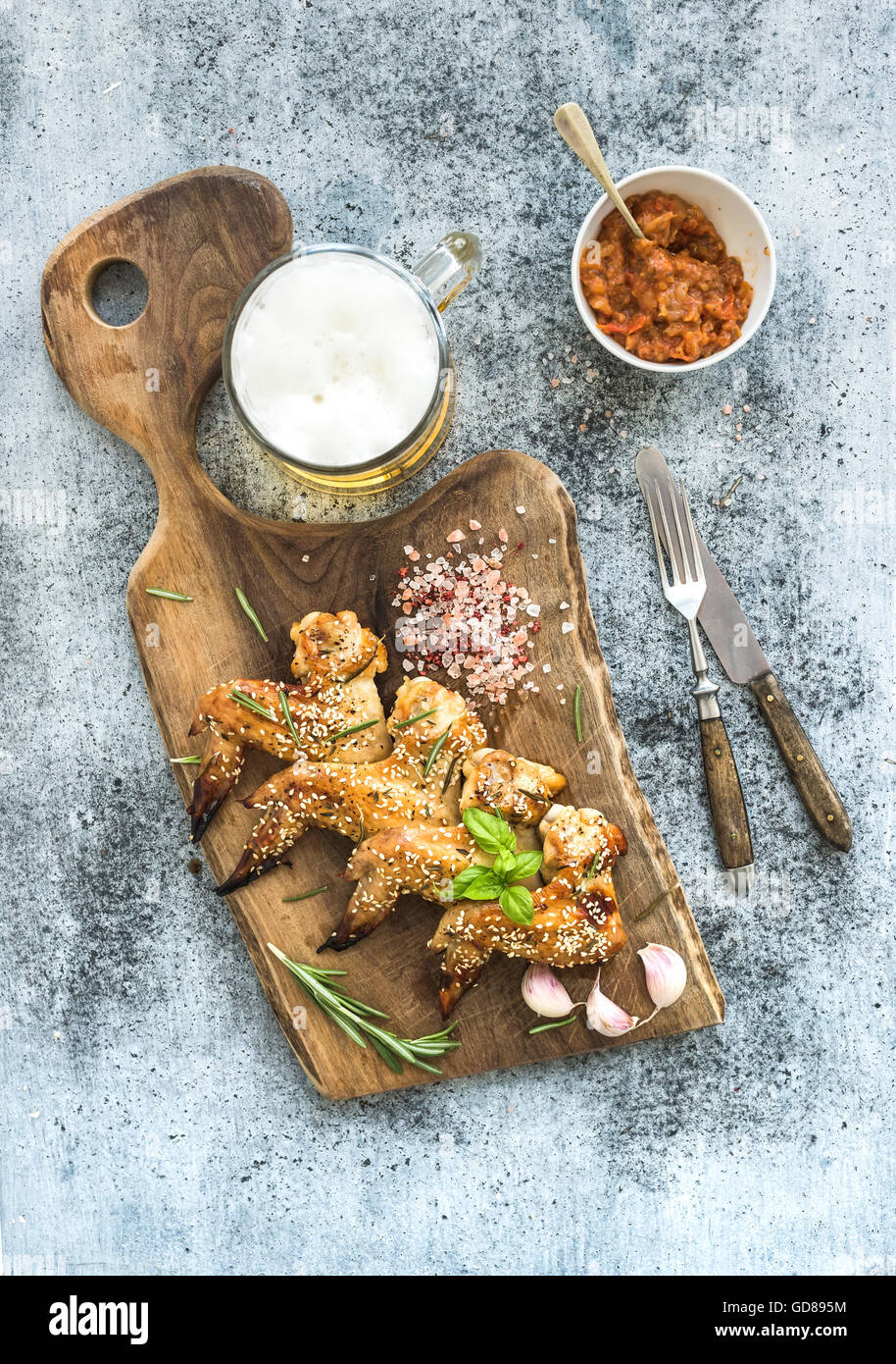 Grilled chicken wings with seasam, spices and herbs, glass of beer and tomato sauce on rustic wooden board over light concrete b Stock Photo