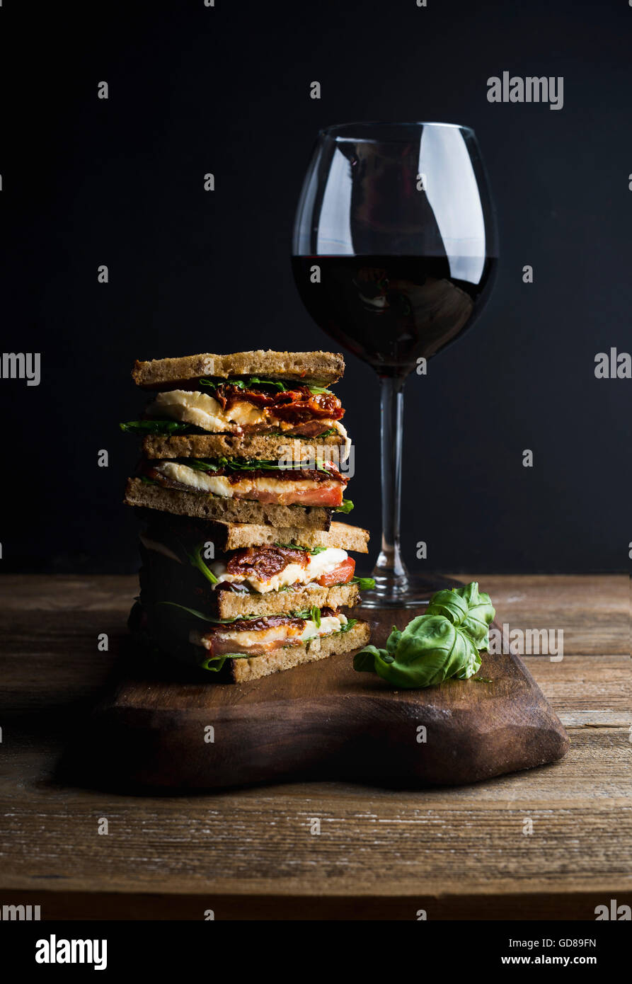 Caprese sandwich or panini with whole grain bread, mozzarella, cherry and dried tomatoes, basil served with glass of red wine on Stock Photo