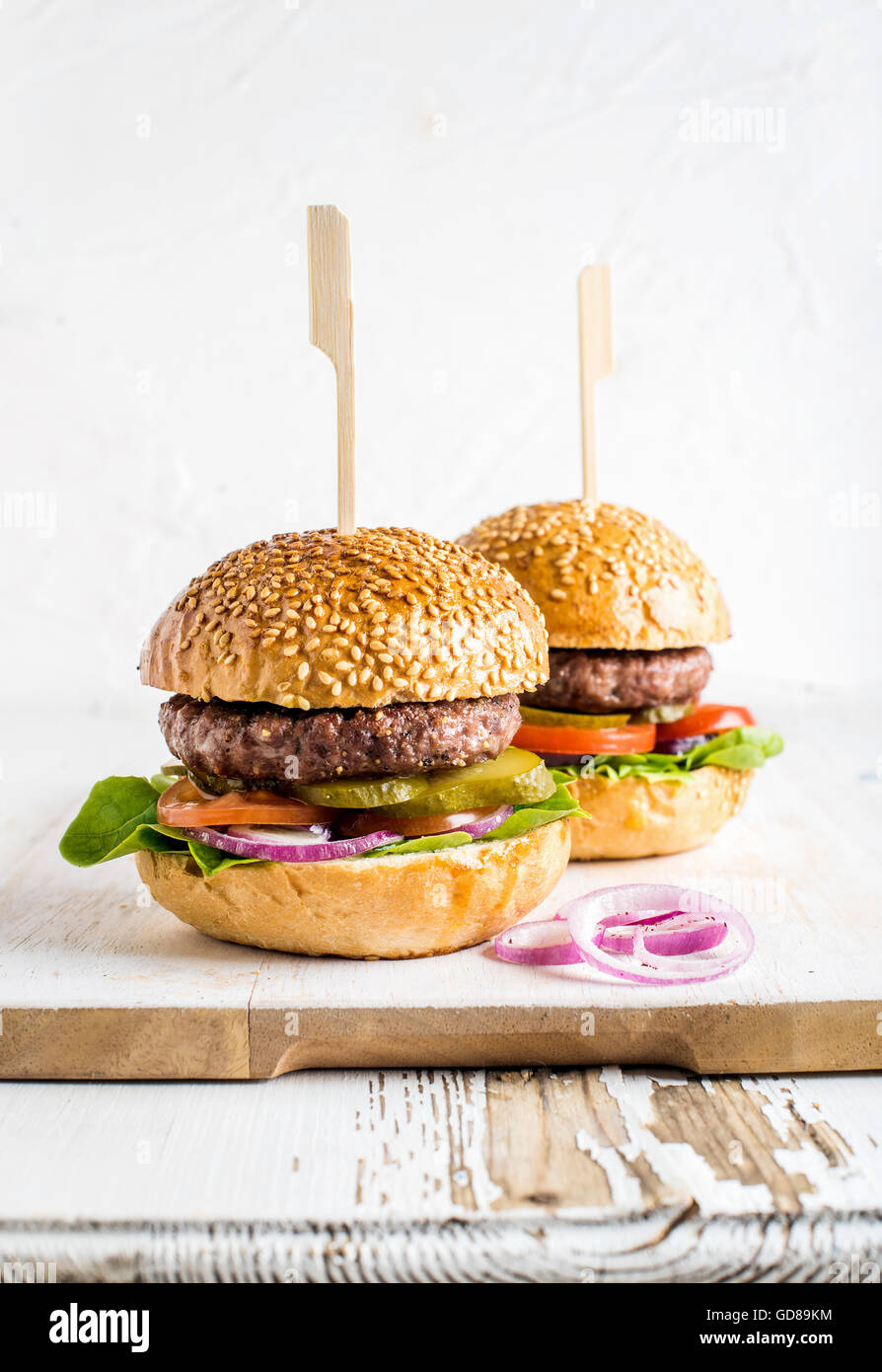 Two fresh homemade burgers served with onion rings on wooden serving board over white background, selective focus, vertical comp Stock Photo