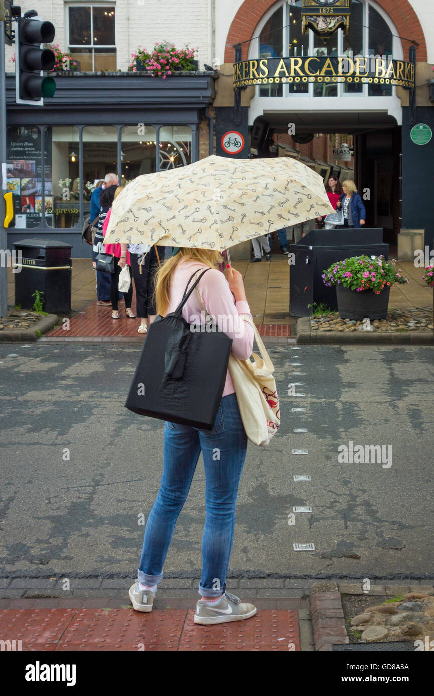 Young woman with an umbrella waiting to cross the road in a Yorkshire Town Centre Stock Photo