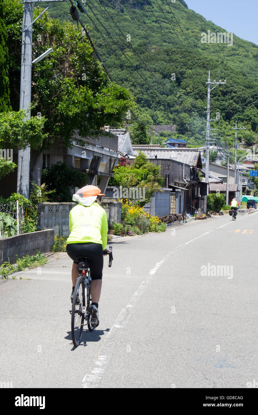 Two touring cyclists riding on a country road past a traditional Japanese village on Shodo Island. Stock Photo